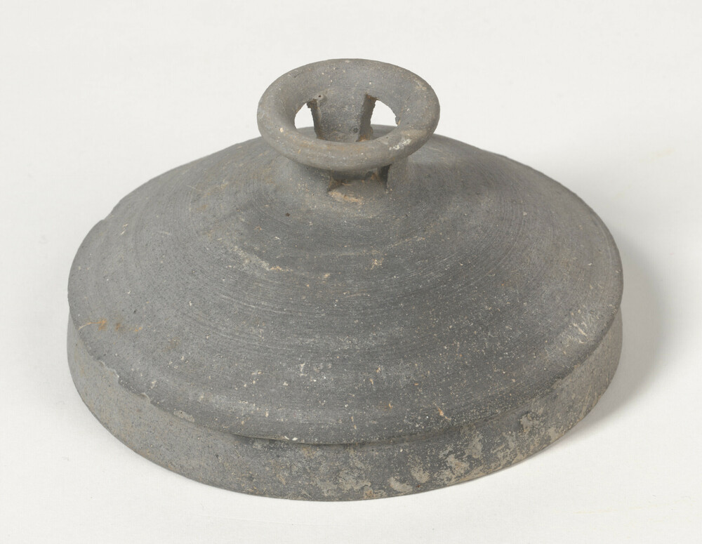 Ceramic 2 of 2 titled Lid with pierced knob, unglazed buff stoneware, reduction-fired dark gray, accession number 2004.9.5.