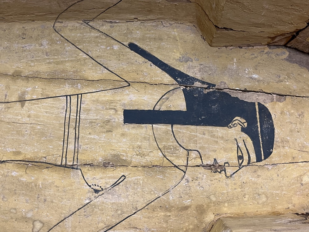 Hearst Museum object 109 of 167 titled Coffin, accession number 6-19912, described as Wooden anthropoid coffin. Inscription running down center of lid. Determined by Kea Johnston to probably be the outer coffin of Iwefaa (6-19928, 12-11039). According to Kea Johnston, "This coffin belonged to a man named Iwefaa, whose name is inserted in the middle of the spells written in the two columns on the front. This coffin is likely the outer coffin for PAHMA 6-19928 based on the similarity of the owner's name, unusual costume, and the paleography of the inscription. Both coffins were purchased on the antiquities market by George Reisner for Phoebe A Hearst. However, stylistically, they are very similar to a set of coffins known to have come from the site of Akhmim, which was excavated in the 1880s by Gaston Maspero, and which has heavily looted for the antiquities market during this decade." "The pectoral vignette between the text and the collar shows the deceased standing before squatting baboon and is the source of our logo. The hieroglyph for 'sky' is above their heads, and the side borders are formed by a pyramid and the symbol for the West.