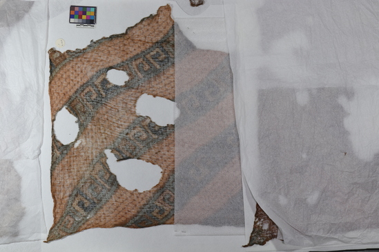 Hearst Museum object titled Cloth fragment, accession number 16-2018, described as Slightly less fragmentary piece of similar fabric with elaborate angular volute design in diagonal bands; design in blue and green upon a brown field; a very fine piece.