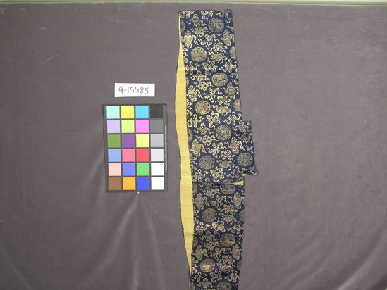 Hearst Museum object titled Textile fragment, accession number 9-15585, described as Fragment of garment; silk, flat gilt paper strips; satin weave, brocaded, plain weave lining; dark blue ground, gold designs, yellow lining; dragon, Buddhist symbol motives; 6 1/2 in. x 37 1/2 in.