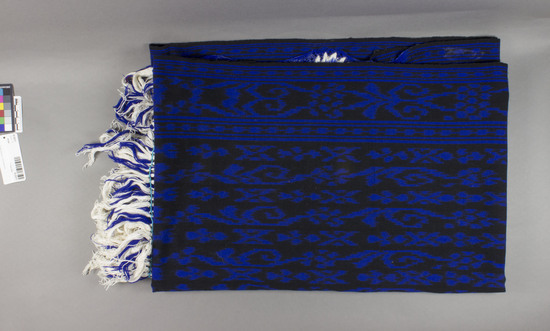 Hearst Museum object 1 of 2 titled Shawl, accession number 16-20211, described as Shawl; 76 x 145 cm, excluding knotting and fringe; ikat; black ground with blue ikat figures; starched royal blue knotting 35 cm l. with warp fringe plus added threads; embroidered flowres, leaves, and butterflies throughout knotted area in bright blue, turquoise, and white; silver sequins french knotted to flowers, leaves and butterflies;