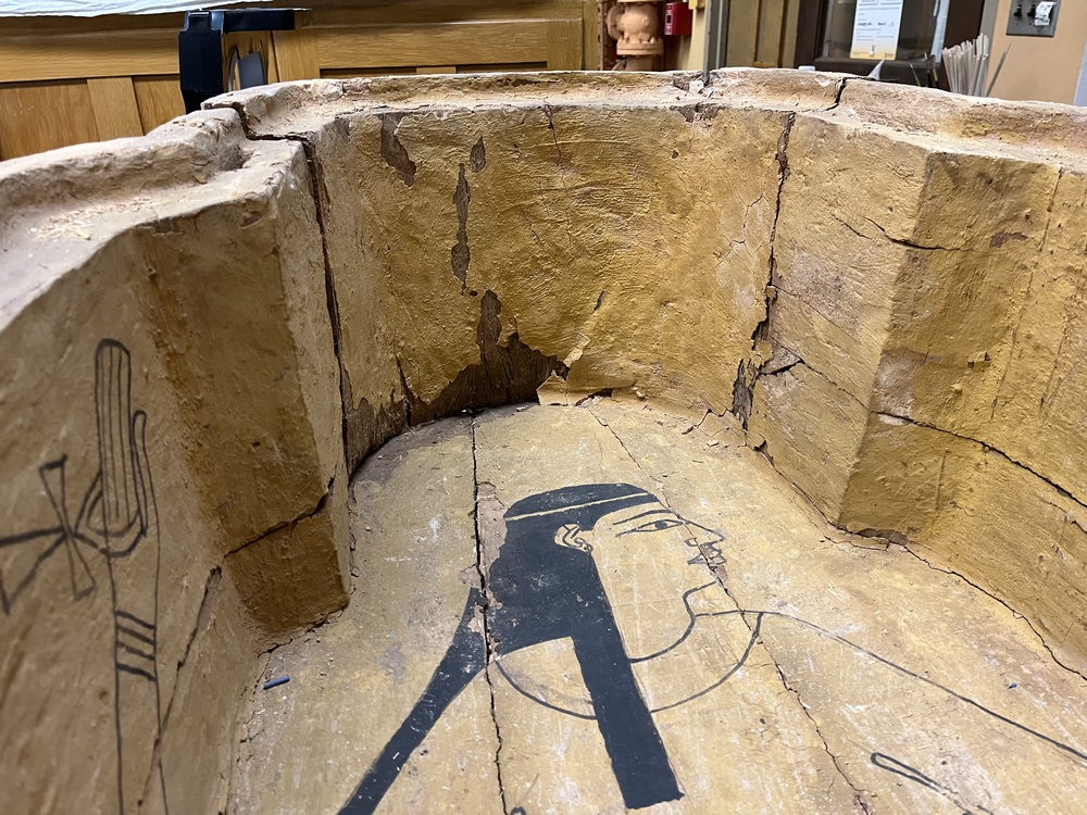 Hearst Museum object 125 of 167 titled Coffin, accession number 6-19912, described as Wooden anthropoid coffin. Inscription running down center of lid. Determined by Kea Johnston to probably be the outer coffin of Iwefaa (6-19928, 12-11039). According to Kea Johnston, "This coffin belonged to a man named Iwefaa, whose name is inserted in the middle of the spells written in the two columns on the front. This coffin is likely the outer coffin for PAHMA 6-19928 based on the similarity of the owner's name, unusual costume, and the paleography of the inscription. Both coffins were purchased on the antiquities market by George Reisner for Phoebe A Hearst. However, stylistically, they are very similar to a set of coffins known to have come from the site of Akhmim, which was excavated in the 1880s by Gaston Maspero, and which has heavily looted for the antiquities market during this decade." "The pectoral vignette between the text and the collar shows the deceased standing before squatting baboon and is the source of our logo. The hieroglyph for 'sky' is above their heads, and the side borders are formed by a pyramid and the symbol for the West.