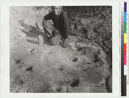 Hearst Museum object titled Black-and-white negative, accession number 15-2761, described as A near view of the mortar stone with Captain McKenzie about to illustrate the process of grinding