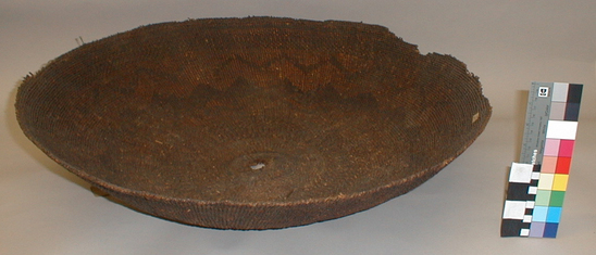 Hearst Museum object titled Flat basket, accession number 1-11657, described as Flat basket; twined. Warp is Hazel (Corylus cornuta californica), weft is Sugar pine (Pinus lambertiana). Meal basket. extremely grimy and smoke blackened from use. Small hole in center. Rim ragged. 2 splits. Plain twined. White single faced overlay