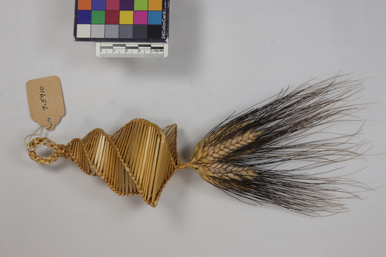 Hearst Museum object titled Corn dolly, accession number 7-5910, described as Corn dolly; wheat straw, plaited; conical shape; square closed bottom with tuft of black-bearded wheat heads hanging from the center; braided loop at top; length 29 cm.