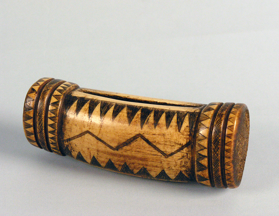 Hearst Museum object titled Money purse, accession number 1-1219, described as Elk antler, hollow, longitundinal slit at center for insertion of dentalium shells; elaborate isosceles triangular, zigzag, and crosshatch design. Double groove near each end.