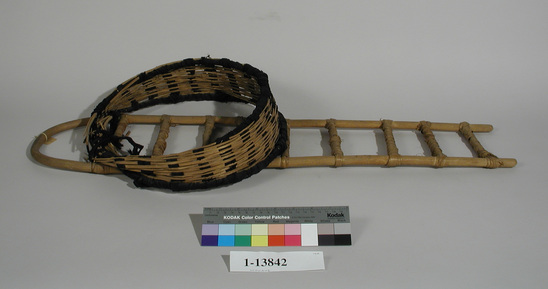 Hearst Museum object 1 of 2 titled Cradle, accession number 1-13842, described as Frame work and head covering of cradle.  The frame is said to be made of mesquite root.  Black textile material interwoven through head covering.