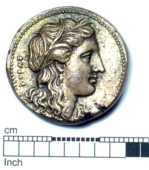 Hearst Museum object titled Coin: ar, accession number 8-5532, described as Coin; AR; Tetradrachm; Greek. 13.69 grams, 25 mm. 310-304 BC. Syracuse, Sicily. Obverse: ΚΟΡΑΣ, head of Kore r. Reverse: ΛΓΑΟΟΚΑΕΙΟΣ, Nike at trophy, Triskeles to right of trophy  Remarks: “Euboic-Attic Standard” "(green coppery discoloration, and a “pinhole”, on the Nike)