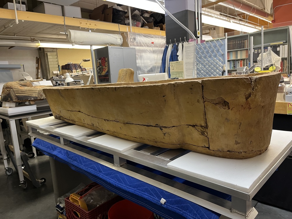 Hearst Museum object 138 of 167 titled Coffin, accession number 6-19912, described as Wooden anthropoid coffin. Inscription running down center of lid. Determined by Kea Johnston to probably be the outer coffin of Iwefaa (6-19928, 12-11039). According to Kea Johnston, "This coffin belonged to a man named Iwefaa, whose name is inserted in the middle of the spells written in the two columns on the front. This coffin is likely the outer coffin for PAHMA 6-19928 based on the similarity of the owner's name, unusual costume, and the paleography of the inscription. Both coffins were purchased on the antiquities market by George Reisner for Phoebe A Hearst. However, stylistically, they are very similar to a set of coffins known to have come from the site of Akhmim, which was excavated in the 1880s by Gaston Maspero, and which has heavily looted for the antiquities market during this decade." "The pectoral vignette between the text and the collar shows the deceased standing before squatting baboon and is the source of our logo. The hieroglyph for 'sky' is above their heads, and the side borders are formed by a pyramid and the symbol for the West.