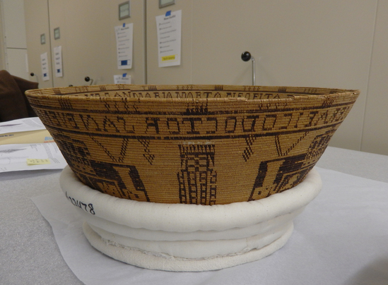 Hearst Museum object 13 of 27 titled Presentation basket, accession number 1-22478, described as Chumash coin-design presentation basket made by María Marta Zaputimeu, early 1800s. Three-rod juncus foundation is sewn with finely split sumac, black-dyed juncus, and a small amount of natural-orange juncus in the base design. The interior of the basket features the coat of arms of the Spanish kings repeated four times. This design was copied from a Spanish colonial coin known as the pillar dollar or piece of eight. The inscription reads "MARIA MARTA NEOFITA DE LA MISION DE EL SERAFICO DOCTOR SAN BVENAVENTVRA ME HIZO AN" (Maria Marta, neophyte of the mission of the Seraphic Doctor San Buenaventura made me [in the year]).  According to Timbrook (2014), "María Marta Zaputimeu (also spelled Saputimehue) was a Chumash woman born at the village of S'omɨs, namesake of the present-day town of Semis. She was baptized at nearby Mission San Buenaventura on June 5, 1788, at about twenty-one years of age (Mission San Buenaventura 1782-1808:No. 363). She had no children and died in 1830." According to Timbrook (2014), close inspection reveals "that fluffy white feathers were inserted horizontally into the foundation on the nonwork face, as the basket was being woven. These appear only on the exterior and are associated only with the four vertical pillarlike design elements that alternate with the shield figures." According to Timbrook, the incorporation of feathers was a stunning departure from Chumash tradition: "this use of feathers is more like that seen in Ohlone and Pomo examples.... and until now has been completely unknown in Chumash basketry."  Diameter: approximately 16¼ inches; height: 6½ inches. About 320 weft strands per inch. Notice: Image restricted due to its potentially sensitive nature. Contact Museum to request access.