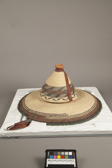 Hearst Museum object titled Basketry hat, accession number 5-3095, described as Basketry hat; Malfa; fiber, wide brim; cone shaped top; multi-colored decoration, black, red green; red leather chin strap.