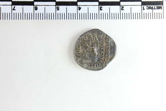 Hearst Museum object titled Coin, accession number 9-22807, described as Parthian coin, silver, tarnished; recto: face in profile facing right, long beard, diadem on head with end hanging down, earring; verso: seated figure with bow surrounded by "text" made of dots.