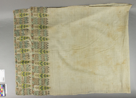 Hearst Museum object titled Mortuary towel, accession number 9-15010, described as Mortuary towel.  Cotton, silk, flat metal strips.  Plain weave, embroidered.  Natural ground, varicolored designs.  Variation of "mosque and cyprus" motives.  53 inches by 21 inches.