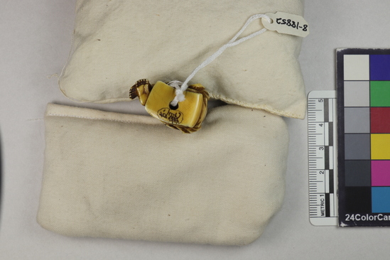 Hearst Museum object titled Netsuke, accession number 9-18852, described as Netsuke; seated "gate man;" bonnet or skull cap tied under chin; both legs drawn up and feet crossed; seated on extension of robe; wrinkled brow and smiling ace; H 3.4 cm X W 3.1 cm