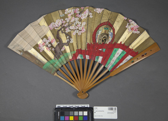 Hearst Museum object titled Fan, accession number 9-16166, described as Paper fan; with bamboo ribbing; one side painted with gold background, two birds and large tree with pink blossoms; opposite side has green background with gold flecks and a continuation of pink blossoms. Bamboo ribs have holes cut into them and are used to make musical sounds.