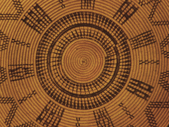 Hearst Museum object 5 of 27 titled Presentation basket, accession number 1-22478, described as Chumash coin-design presentation basket made by María Marta Zaputimeu, early 1800s. Three-rod juncus foundation is sewn with finely split sumac, black-dyed juncus, and a small amount of natural-orange juncus in the base design. The interior of the basket features the coat of arms of the Spanish kings repeated four times. This design was copied from a Spanish colonial coin known as the pillar dollar or piece of eight. The inscription reads "MARIA MARTA NEOFITA DE LA MISION DE EL SERAFICO DOCTOR SAN BVENAVENTVRA ME HIZO AN" (Maria Marta, neophyte of the mission of the Seraphic Doctor San Buenaventura made me [in the year]).  According to Timbrook (2014), "María Marta Zaputimeu (also spelled Saputimehue) was a Chumash woman born at the village of S'omɨs, namesake of the present-day town of Semis. She was baptized at nearby Mission San Buenaventura on June 5, 1788, at about twenty-one years of age (Mission San Buenaventura 1782-1808:No. 363). She had no children and died in 1830." According to Timbrook (2014), close inspection reveals "that fluffy white feathers were inserted horizontally into the foundation on the nonwork face, as the basket was being woven. These appear only on the exterior and are associated only with the four vertical pillarlike design elements that alternate with the shield figures." According to Timbrook, the incorporation of feathers was a stunning departure from Chumash tradition: "this use of feathers is more like that seen in Ohlone and Pomo examples.... and until now has been completely unknown in Chumash basketry."  Diameter: approximately 16¼ inches; height: 6½ inches. About 320 weft strands per inch. Notice: Image restricted due to its potentially sensitive nature. Contact Museum to request access.