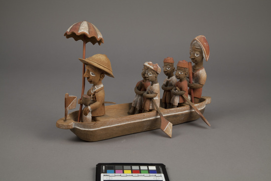 Hearst Museum object titled Figures, accession number 5-16237a-q, described as caricature figure group; caricature of a District Officer on tour; carved & painted wood a - boat, has bag of frags b - Dist. officer (front) c - poler (rear) d - paddler (LF) e - paddler (LR) f - paddler (RF) g - paddler (RR) h - hat i - umbrella handle j - umbrella k - flag l - pipe m - pole n - paddle (RF) o - paddle (LF) p - paddle (LR) q - paddle (RR) Found two pegs in a bag with this object number.