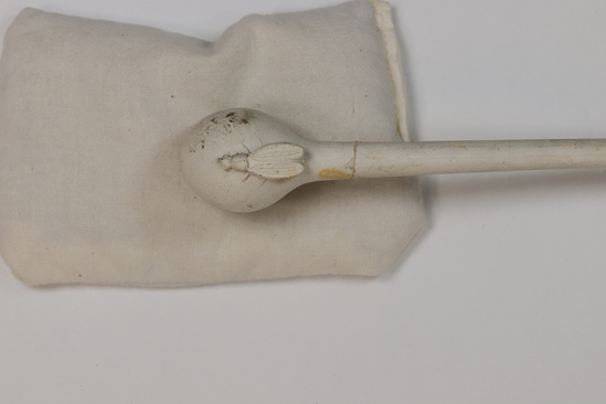 Hearst Museum object 3 of 6 titled Pipe w/ box, accession number 7-9664a-c, described as Pipe with box. (a) Pipe, white clay, long stem, foot with full relief of a bee, incised “Gambie a Paris m * M Depose 1079;” broken. Length 20 cm. Diameter of bowl 2.5 cm. (b), (c) Box, two pieces, wood, with brass catch, stained, broken. Length 22 cm. Diameter of bowl 3 cm.