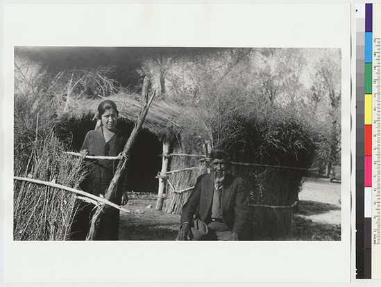 Hearst Museum object titled Black-and-white negative, accession number 15-7769, described as Mrs. Shelton (left) and Francisco Nombrie sitting in front of ceremonial house.