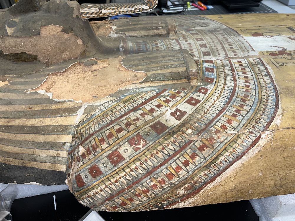 Hearst Museum object 34 of 167 titled Coffin, accession number 6-19912, described as Wooden anthropoid coffin. Inscription running down center of lid. Determined by Kea Johnston to probably be the outer coffin of Iwefaa (6-19928, 12-11039). According to Kea Johnston, "This coffin belonged to a man named Iwefaa, whose name is inserted in the middle of the spells written in the two columns on the front. This coffin is likely the outer coffin for PAHMA 6-19928 based on the similarity of the owner's name, unusual costume, and the paleography of the inscription. Both coffins were purchased on the antiquities market by George Reisner for Phoebe A Hearst. However, stylistically, they are very similar to a set of coffins known to have come from the site of Akhmim, which was excavated in the 1880s by Gaston Maspero, and which has heavily looted for the antiquities market during this decade." "The pectoral vignette between the text and the collar shows the deceased standing before squatting baboon and is the source of our logo. The hieroglyph for 'sky' is above their heads, and the side borders are formed by a pyramid and the symbol for the West.