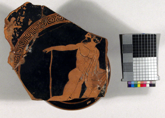 Hearst Museum object titled Kylix fragments, accession number 8-2183, described as Attic Red-figure kylix; foot, stem and a little of the bowl preserved; ancient rivet holes; I, bearded komast looking to left but moving to right (stick, wreath, cloak, and cup); maeander border; exterior: something remains of one figure of each side: part of main in cloak moving to right; part of another figure in motion; palmettes at handles.