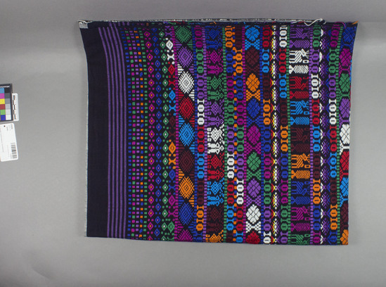 Hearst Museum object titled Textile, accession number 3-30226, described as RGM yardage, 35 inches width and 80 inches long; wide (18 1/2 inches of grey (made up of black and white threads) form first band across width; next band is black, then narrow purple and black stripes, followed by colorful dots on black, then flowers (?) on black; the rest of the bands up to the center (where it reverses) includes larger flowers (?),  "I" and O" repeats, man and bird repeat, more "I" and "O" repeats, flowers, and eventually a band of rain deer and tree repeats.