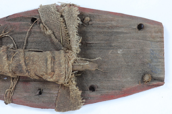 Hearst Museum object titled Crocodile mummy tail, accession number 6-21629d, described as Tail of crocodile mummy on red-painted wood platform. tail consists of wood wrapped with linen strips that also attach it to the platform. Wood platform has peg holes, some with pegs, along side edges. Length of tail: 12.2 cm; length of platform: 12 cm.