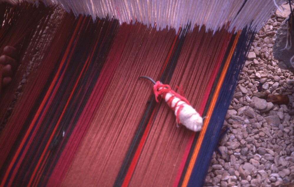 Hearst Museum object titled Color slide, accession number 25-99060, described as 35mm color slide transparency: "Tarfa's shisa + heddles, w". Close-up of a loom on the ground with a tool on it.