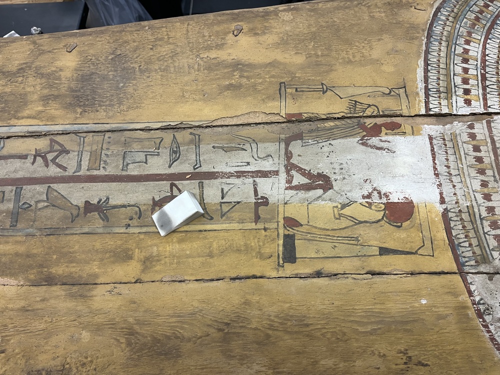 Hearst Museum object 130 of 167 titled Coffin, accession number 6-19912, described as Wooden anthropoid coffin. Inscription running down center of lid. Determined by Kea Johnston to probably be the outer coffin of Iwefaa (6-19928, 12-11039). According to Kea Johnston, "This coffin belonged to a man named Iwefaa, whose name is inserted in the middle of the spells written in the two columns on the front. This coffin is likely the outer coffin for PAHMA 6-19928 based on the similarity of the owner's name, unusual costume, and the paleography of the inscription. Both coffins were purchased on the antiquities market by George Reisner for Phoebe A Hearst. However, stylistically, they are very similar to a set of coffins known to have come from the site of Akhmim, which was excavated in the 1880s by Gaston Maspero, and which has heavily looted for the antiquities market during this decade." "The pectoral vignette between the text and the collar shows the deceased standing before squatting baboon and is the source of our logo. The hieroglyph for 'sky' is above their heads, and the side borders are formed by a pyramid and the symbol for the West.