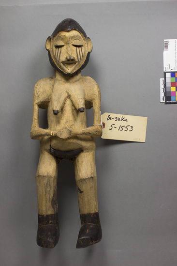 Hearst Museum object titled Figurine, accession number 5-1553, described as Carved wooden figurine, Suku “fetish;” Mbambi (Northeast Baasuku). Height 48.23 cm. Mbambi figurine. Carved by a man from Mungulu village of Secteur Pay, Territoire Masi-Manimba. The manwas regarded as a good sculptor by the Suku. Figurine is part of the paraphernalia of the “war medicine” Mbambi. The medicine was first introduced shortly before 1920, by the Suku king from the Bambala to the north. It was given to groups of elders in each chieftaincy who constituted a kind of “policeforce” led by local political chief or his representative. Every member of the police society was responsible for enforcing peace and order in his vicinity; he had the right to collect fines from those creating disorders (fines shared by all the other policemen of the chieftaincy), and could count upon the help of other members of the police-society in case of resistance by wrong-doers.