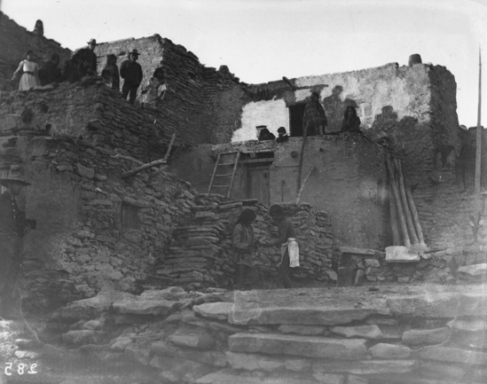 Hearst Museum object titled Black-and-white negative, accession number 15-285, described as Winner of snake race returning the meal gourd and sticks after coming back from his corn patch. Priest taking them at edge of snake Kiva