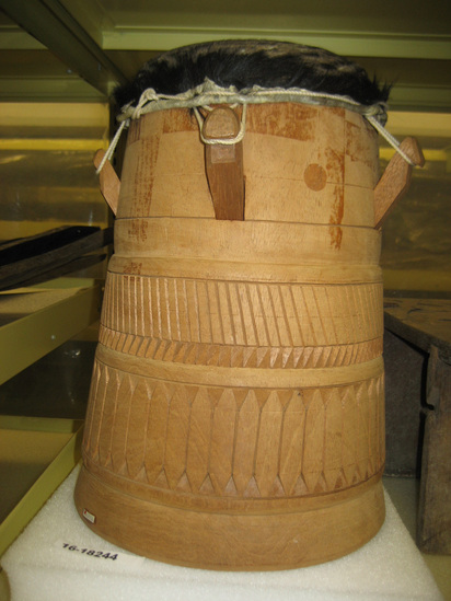 Hearst Museum object titled Drum, accession number 16-18244, described as Wooden ceremonial drum with boarskin top; wood, carved, head of animal hide with black hair, attached to drum with cotton cord that is wrapped around head and wood pegs projecting from drum; circular, geometric design. Carved with traditional Bush Negro design.