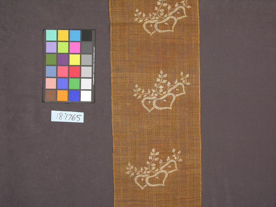 Hearst Museum object titled Textile panel, accession number 18-1765, described as Vegetable fiber in spaced plain weave; brown ground with stenciled or printed ecru floral motif, with blossoms and vine-like branches; panel is hemmed at one end with rod casing at the other.