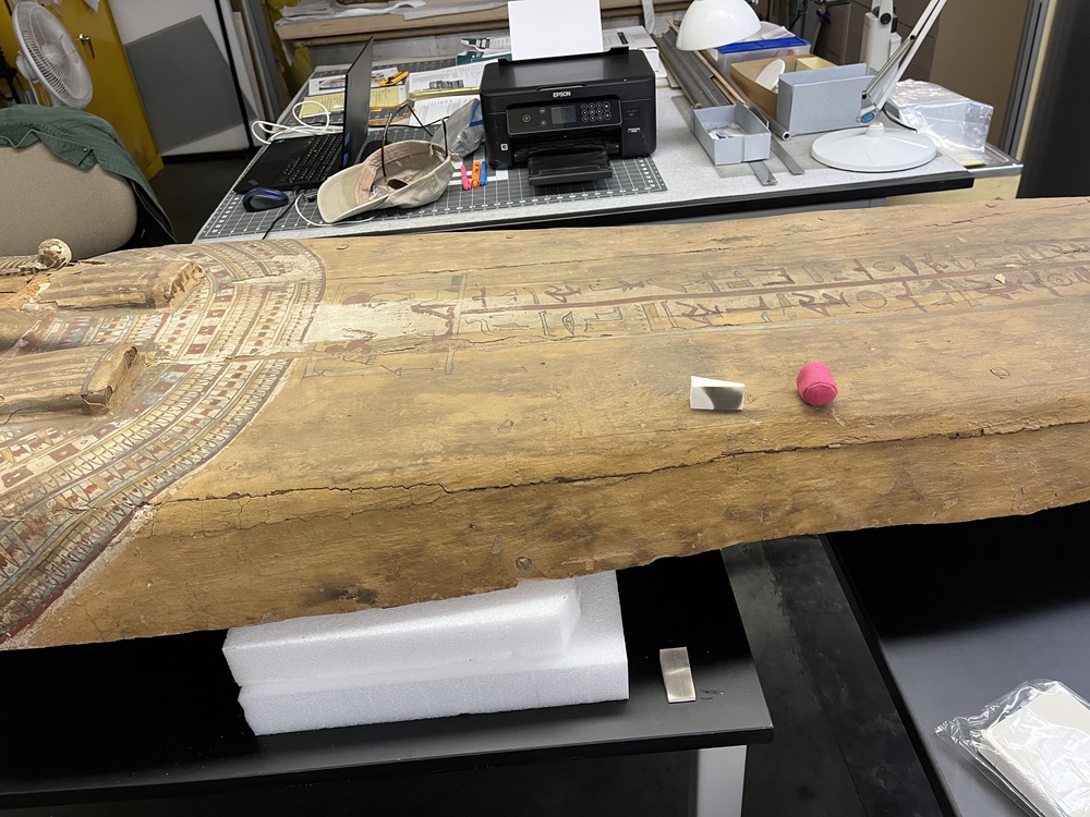 Hearst Museum object 91 of 167 titled Coffin, accession number 6-19912, described as Wooden anthropoid coffin. Inscription running down center of lid. Determined by Kea Johnston to probably be the outer coffin of Iwefaa (6-19928, 12-11039). According to Kea Johnston, "This coffin belonged to a man named Iwefaa, whose name is inserted in the middle of the spells written in the two columns on the front. This coffin is likely the outer coffin for PAHMA 6-19928 based on the similarity of the owner's name, unusual costume, and the paleography of the inscription. Both coffins were purchased on the antiquities market by George Reisner for Phoebe A Hearst. However, stylistically, they are very similar to a set of coffins known to have come from the site of Akhmim, which was excavated in the 1880s by Gaston Maspero, and which has heavily looted for the antiquities market during this decade." "The pectoral vignette between the text and the collar shows the deceased standing before squatting baboon and is the source of our logo. The hieroglyph for 'sky' is above their heads, and the side borders are formed by a pyramid and the symbol for the West.
