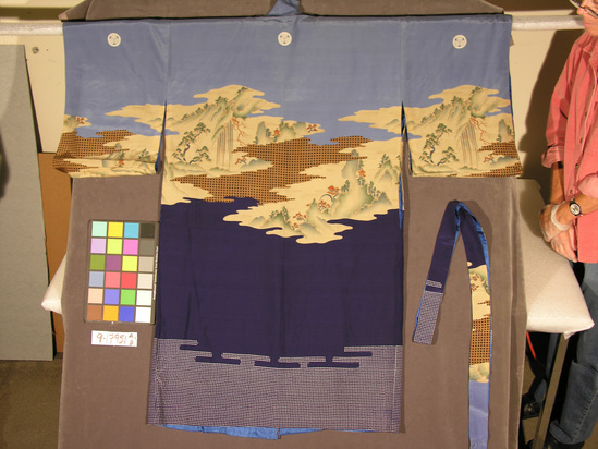 Hearst Museum object titled Textile, accession number 9-17951a,b, described as A) Kimono: silk, plainweave, printed w/ mountain landscapes & checkerboard; predominately indigo & cerelean blue, landscape beige; good condition; fully line in blue silk.  B) Sash, made from a vertical length of same fabric.  Plain weave silk, printing.  A) 131 cm L.  b) 238 cm L.
