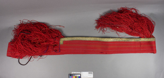 Hearst Museum object titled Sash, accession number 7-5124, described as Woman's wool sash (prepaska); made from homespun; gold braid and red fringe on one side; red fringe at one end' 146 inches long. This sash, made by women for their own use is worn (especially by the younger women) for everyday, but especially sundays and festive occasions, over the pojas. The word prepaka is normally used for a sash loosely tied or a cloth tied as a sash around a child. Glichik the name is used to distinguish it from other type of sash (pojas, 7-5123) also worn. Still worn by some women at time of collection, 1964. 7-5119-5128 comprise a complete costume.