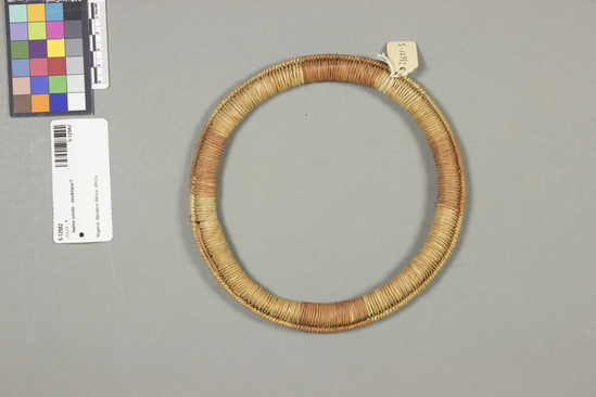 Hearst Museum object titled Twine circle - necklace?, accession number 5-12982, described as Twine circle- necklace?., Africa, Nigeria att. 5-12982, acc no. 2879. File code: 5.6 Collector: T.D. Lanagan. Donor: W.H. Lawson. Materials, techniques: Twisted vegetable fiber wrapped around fiber ring Context of use: Poss. used in ring toss or similar game Description: Ring, prob. part of ring toss or other game; twisted vegetable fiber, some dyed light brown, wrapped around central ring; 17 cm. diameter