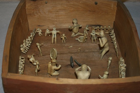 Hearst Museum object titled Dance model, accession number 2-6418, described as Carved bone and ivory models of dancers in box with cover. Includes 2 drummers, 2 soapstone birds. Box exterior stained red. Rawhide hinges.