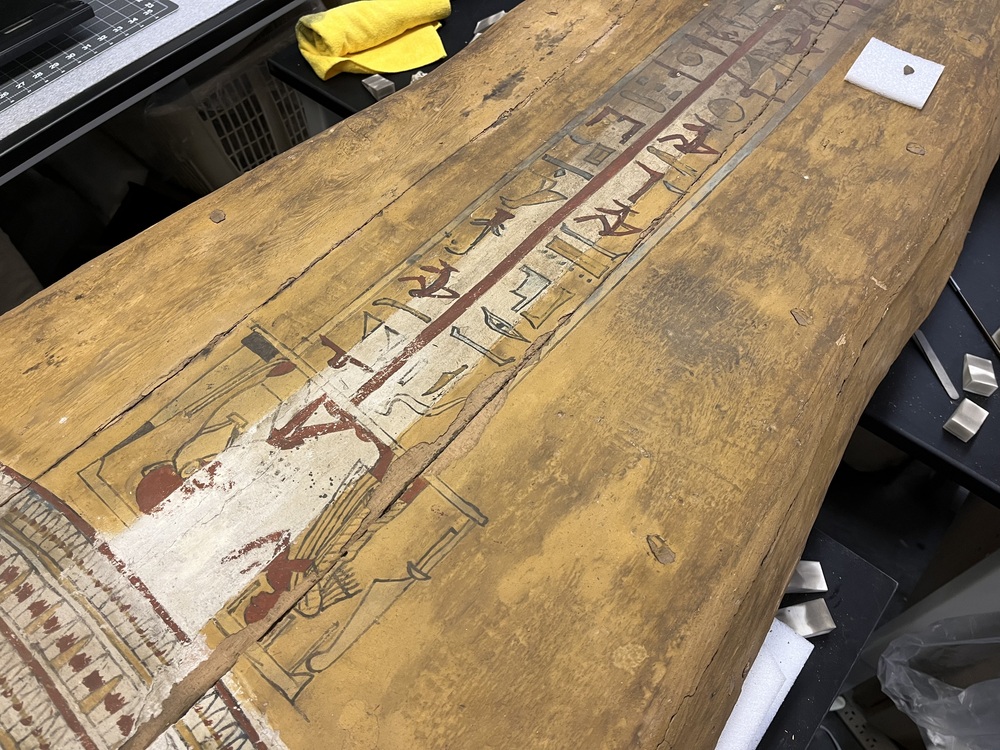 Hearst Museum object 145 of 167 titled Coffin, accession number 6-19912, described as Wooden anthropoid coffin. Inscription running down center of lid. Determined by Kea Johnston to probably be the outer coffin of Iwefaa (6-19928, 12-11039). According to Kea Johnston, "This coffin belonged to a man named Iwefaa, whose name is inserted in the middle of the spells written in the two columns on the front. This coffin is likely the outer coffin for PAHMA 6-19928 based on the similarity of the owner's name, unusual costume, and the paleography of the inscription. Both coffins were purchased on the antiquities market by George Reisner for Phoebe A Hearst. However, stylistically, they are very similar to a set of coffins known to have come from the site of Akhmim, which was excavated in the 1880s by Gaston Maspero, and which has heavily looted for the antiquities market during this decade." "The pectoral vignette between the text and the collar shows the deceased standing before squatting baboon and is the source of our logo. The hieroglyph for 'sky' is above their heads, and the side borders are formed by a pyramid and the symbol for the West.