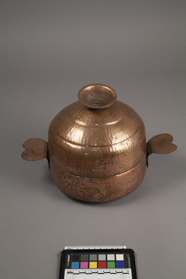 Hearst Museum object titled Chapati bread box, accession number 9-16157a,b, described as Bread container (chapati box): made of hammered copper; Handles shaped like petals at each side. Inverted small bowl forms handle for lid. Box(a) 67cm circumference; and lid (b) 23 cm high. For chapatis, a flat Indian bread. Cost; $30