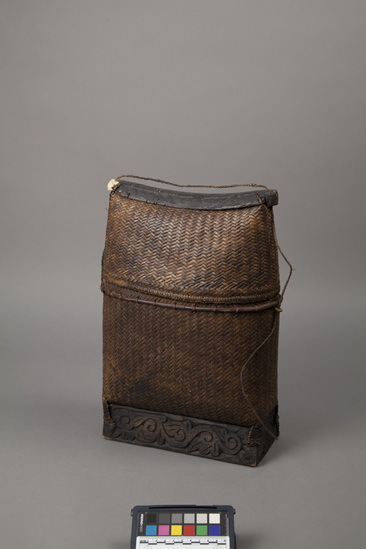 Hearst Museum object titled Basket purse and lid, accession number 18-1358, described as Basket purse, with lid and protective wood base; square, with triangular side view; lid secured with cord which serves as carrying strap. Worn under one arm for carrying personal effects. Total height 40 cm. (a) Basket height 32 cm. (b) Lid height 15 cm.