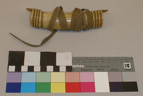 Hearst Museum object titled Money purse, accession number 1-1221a-c, described as (a) Money purse. Antler, hollow, curved; raised flange with 3 grooves at each end; tab at each end. (b) Cover for (a). Antler, rectangular, hole for thong. (c) Thong, wrapped around (a) to secure cover (b).