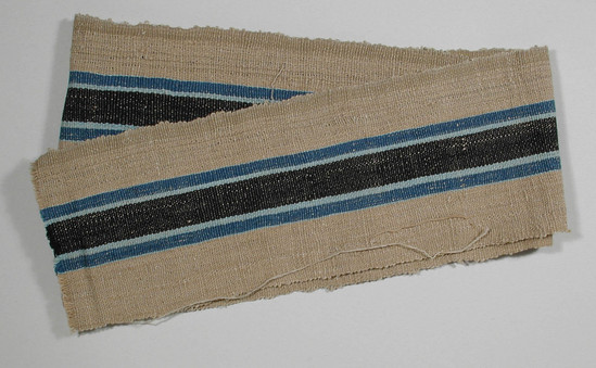 Hearst Museum object titled Textile fragment, accession number 5-11031, described as Textile sample (section of narrow band weaving). Brown beige ground with central black stripe (1.6 cm) flanked by two pale blue and one wider bright blue stripe (.5 cm). Khaki stripe down selvage.