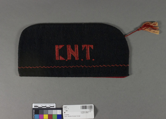 Hearst Museum object titled Cap, accession number 7-6673, described as CAP:  Folds flat on seams joining halves.  One side red, one side black of cotton flannel.  Red side emb. w. "F.A.I." in 1½ inch letters above a black scalloped line.  Black side emb. w. K.N.T." above a red scalloped line.  red and white tassel on cord hangs from top front.  Machine emb.  Cotton flannel.  Embroidery.  Red and black.  Good condition, lined w. coarse black plain weave.  10¾ inches by 5 inches.