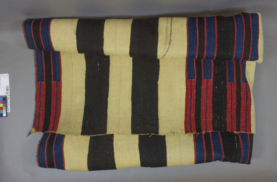 Hearst Museum object titled Blanket, accession number 2-58505, described as Chief's blanket," Second Phase; top, center and bottom bands are dark brown, red (cochineal-dyed bayeta), and indigo with indigo blocks on cochineal ground; there are ten alternating white and brown bands on the body of the blanket (5 above and 5 below the center band); all handspun except for red (1-ply unraveled bayeta); green wool selvedge; tapestry weave.