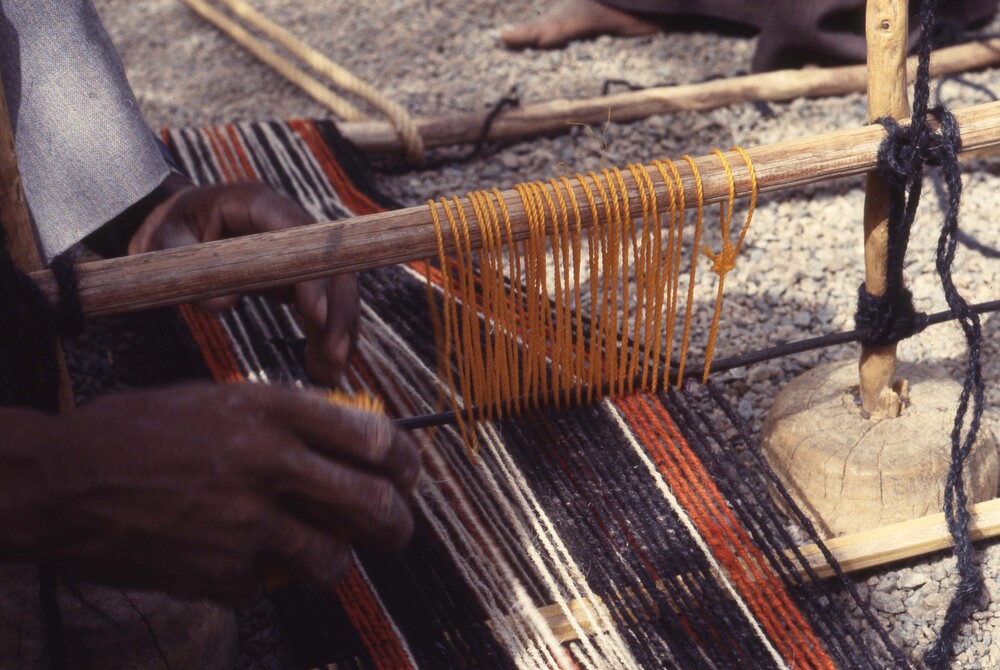Hearst Museum object titled Color slide, accession number 25-98445, described as 35mm color slide transparency. Close-up of a person weaving on a loom on the ground.