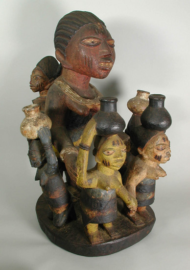 Hearst Museum object titled Figurines, accession number 5-13702, described as Figurines/shrine piece. Standing woman w/ baby on back; her arms extended to 2 standing women; 2 kneeling women near her sides; the 4 smaller women each have water container on head; self base; wood painted dark brown, red and yellow;  h. larger women ca. 67 cm.