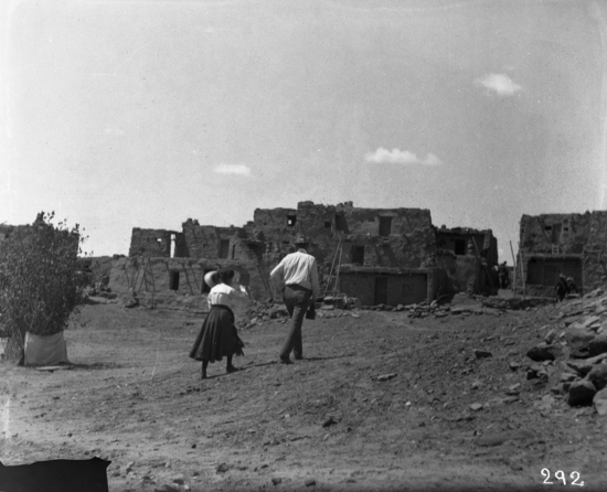 Hearst Museum object titled Black-and-white negative, accession number 15-292, described as White man and woman crossing plaza of Snake dance; buildings in background.