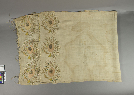 Hearst Museum object titled Grave cloth, accession number 9-15022, described as Grave cloth.  Silk?  Plain weave, embroidered borders.  Unbleached white ground, brown, green, white, yellow, gold and pink designs.  Has irregular fringe.  Gold wrapped yarn used.  18 inches by 42 inches.