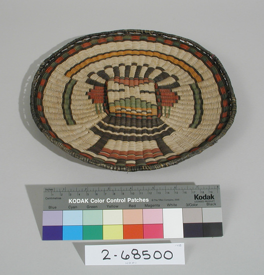 Hearst Museum object 1 of 3 titled Plaque, accession number 2-68500, described as Round, design showing kachina mask using black, red, green and orange on whitened, natural ground. Wicker weave, sumac warp, dyed rabbit brush weft, yucca for wrapped rim.